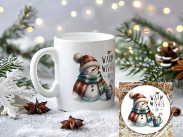 Weihnachtstasse mit Schneemann in warmem Schal und Mütze, der eine Tasse heiße Schokolade mit Zuckerstange hält, begleitet vom Schriftzug 'Warm Wishes'. Perfektes Geschenk für kalte Wintertage und die Weihnachtszeit, mit festlicher Dekoration im Hintergru